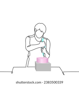 man stands holding culinary bag and squeezing cream out of it onto cake on stand in front of him - one line art vector. concept pastry chef, homemade cake, custom cake, preparation and decoration