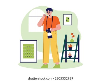 Man stands indoors with a camera hanging around his neck, next to a small shelf unit with plants.