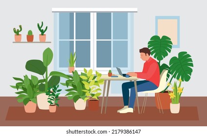 Man staying home working with laptop sitting in the bean bag chair. A room full of plants. Freelance worker in green interior