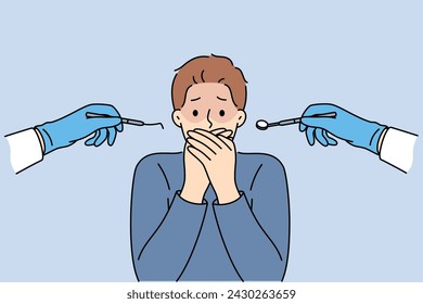 Man suffering from dentophobia closes mouth and stands near hands with dental devices. Guy is afraid of doctors at dental clinic, and feels panic, not allowing caries to be treated