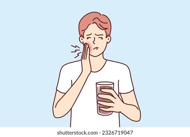 Man suffers from toothache caused by cold drink and needs pain medication and dentist. Guy with toothache associated with caries or stomatitis holds glass of medicine for mouthwash.