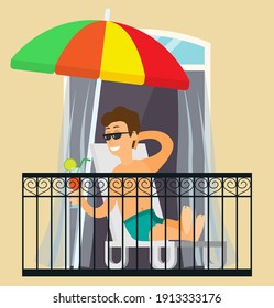 A man sunbathing, resting on the balcony, lies with a cocktail in hands on a sun lounger under an umbrella. Enjoying summer season from balcony of apartment or hotel room. Fun sunbathe activity indoor