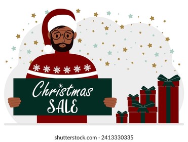A man in a sweater and a red Santa hat holds a poster with the text about Christmas sale in his hand.