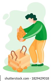 A man takes a large almond out of a wooden box. A handful of almonds and walnuts lie next to the container for nuts. Guy is preparing organic free diary drink. Making natural vegan products