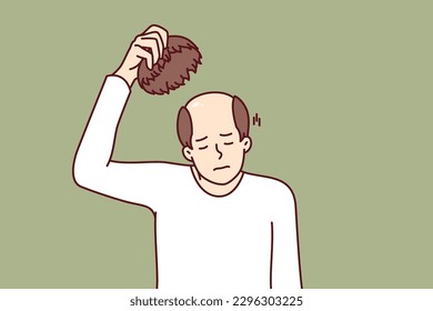 Man takes off wig and experiences stress of baldness caused by health problems or aging. Unhappy adult human with wig in hand needs hair transplant operation or drug to restore hair.