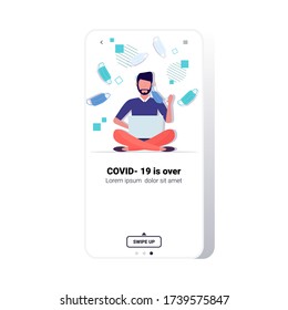 man taking off face mask guy sitting lotus pose using laptop victory over coronavirus pandemic quarantine covid-19 is ending concept smartphone screen mobile app copy space full length vector
