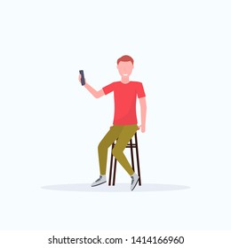 Man taking selfie photo on smartphone camera.  Casual male cartoon character sitting on chair posing. White background, flat full length.