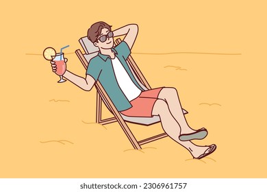 Man tourist is sunbathing on beach sitting in sun lounger and drinking fruity refreshing cocktail. Guy tourist and travel lover sunbathes spending vacation on beach of sunny ocean. 