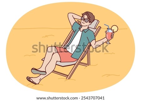 Man tourist is sunbathing on beach sitting in sun lounger and drinking fruity refreshing cocktail. Guy tourist and travel lover sunbathes spending vacation on beach of sunny ocean.
