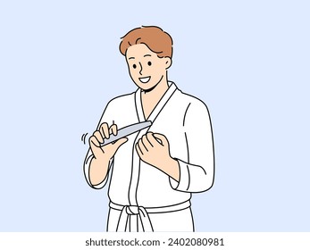 Man uses nail file after shower, performing daily hygiene and SPA procedures to take care of skin. Young cheerful guy holds nail file in hands and looks forward smiling standing in bathrobe