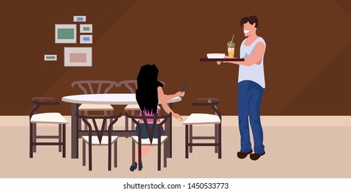 man waiter serving food to woman guest sitting at cafe table modern restaurant interior flat horizontal full length