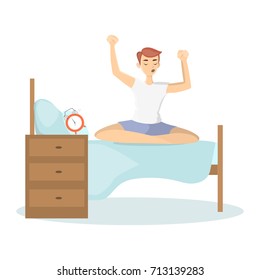 Man waking up. Young sleepy man sits on bed stretching arms.