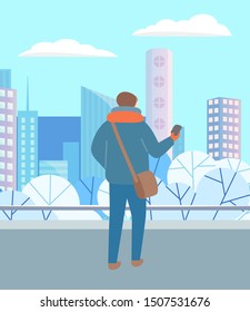 Man walking through urban winter park alone. Person in warm clothes, hat and scarf standing with telephone in hand. Beautiful snowy landscape of city on background. Vector illustration in flat style