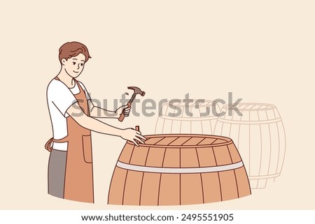 Man winemaker opens barrel with finished drink to taste bordeaux made from organic grapes. Guy is standing in wine cellar, hammering barrel of sherdane to infuse and impart unique smell to wine.