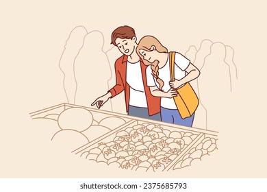 Man and woman do shopping at market and stand near crates of vegetables at farmers fair. Happy couple chooses organic vegetables and fruits to cook delicious food with eco ingredients