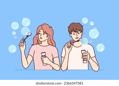 Man and woman inflate soap bubbles and have fun in free time, enjoying pastime together. Couple of casual teenagers with soap bubbles in hands playing and refusing to do useful things