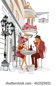 Hombre y mujer sentados y tomando café en un café de la calle. El fondo está decorado con flores y ofrece vistas al casco antiguo.