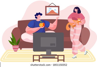 Man and woman young family pet owners at home with a cat, girl holding an animal in her arms, hugging with him. Guy sitting on the sofa front of the TV holding an apple. Owner with her tender kitty