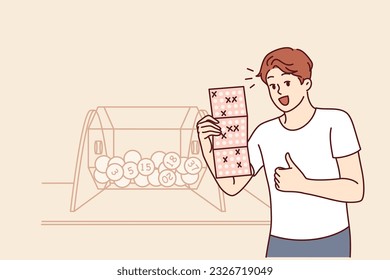 Man won bingo lottery happily demonstrates winning ticket and stands near transparent box with balls. Casino winner jackpot winner showing thumbs up feeling joyful in anticipation of big cash prize