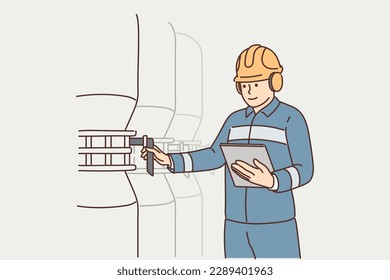 Man working at factory holds electronic tablet standing near industrial equipment and tanks. Employee of industrial company or factory is in boiler room and uses valve to adjust pressure 