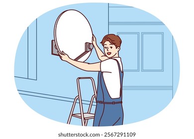 Master installs television satellite dish on facade of building standing on stepladder and looking at screen. TV company specialist sets up access to satellite TV channels for residents house