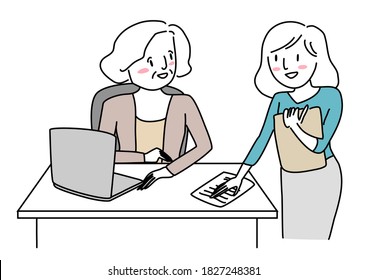Mature businesswoman sitting at desk and talking with young female coworker standing nearby. Young secretary putting paper on manager's desk. Female assistant placing paper sheet on boss's desk.