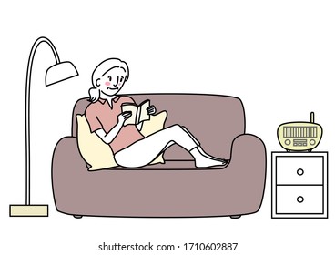 Mature woman sitting on couch and reading book comfortably. Cute senior woman reading book on sofa. Elderly woman enjoying leisure time reading book.