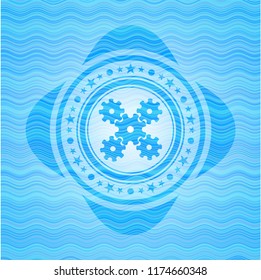 mechanism icon inside light blue water wave style emblem.