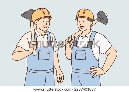 Men in builders uniforms and hardhats hold sledgehammers to demolish wall of emergency building or redevelopment. Guys builders are ready to work on construction site or in renovated room