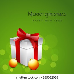 Merry Christmas celebration greeting card or invitation card with gift box wrapped in red ribbon and golden Xmas balls on shiny green background. 