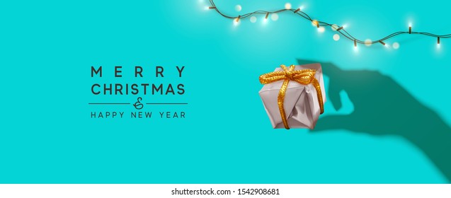 Merry Christmas and Happy New Year. Background with realistic gift box, bright Christmas lights garland. Silhouette shadow from the hands holds Xmas presents. Creative greeting card, holiday banner.