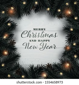 Merry Christmas and Happy New Year design background. Christmas tree branches with light garland and pine cone on wooden texture backdrop. Xmas Flat Lay.