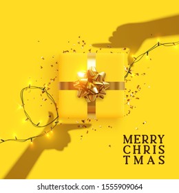 Merry Christmas and Happy New Year. Yellow background with realistic festive gifts box. Effect of the shadow of hands is holding a gift in focus. Photo Frame Hands Made by Young Girls. Xmas present
