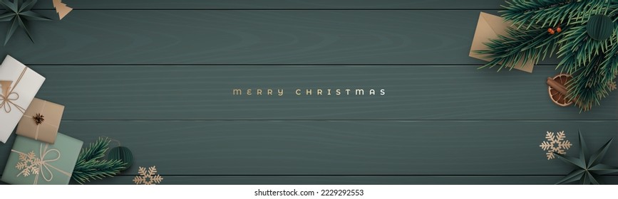 Merry Christmas horizontal banner with fir tree branch, cinnamon, orange slice, berries, gift craft box, envelope and pine cone on dark green wooden floor. Flat lay composition. Rustic style.