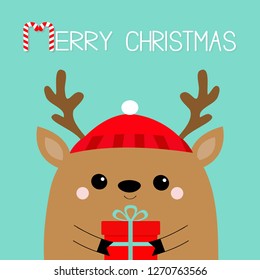 Merry Christmas. Raindeer deer head face holding gift box. Red hat, nose, horns. Happy New Year. Cute cartoon kawaii baby character. Funny animal. Flat design. Hello winter. Blue background. Vector