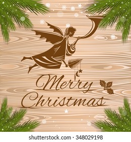 Merry Christmas. The spruce branches and flying angel with a trumpet on a wooden background.