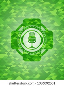 microphone icon inside realistic green emblem. Mosaic background