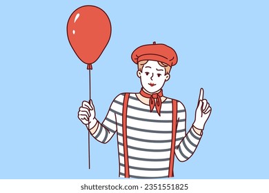 Mime man holding red balloon and pointing finger up, participating in pageant or circus. Mime guy with white face, dressed in long-haired t-shirt and getting ready to make audience laugh