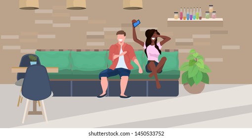 mix race couple sitting on couch man woman using smartphone spending time together people having fun modern cafe interior flat horizontal full length