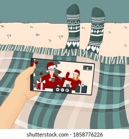 Mobile phone Video call with family or friends on Christmas New Year time. Woman is under the green blue plaid in knitted socks