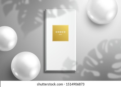 Mockup for advertising chocolate. A flat lay with a packaging and  three shiny white balls and a shadow from the leaves of the Monstera plant