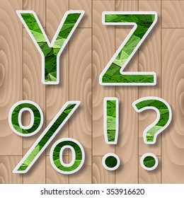 Modern alphabet with shadow effect.Green Leaves font on a wood background.Y,Z letters,punctuation marks,percent