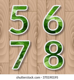 Modern alphabet with shadow effect.Green Leaves font on a wood background. 5,6,7,8 number,digits