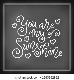 Modern mono line calligraphy lettering of You are my sunshine in white on chalkboard background with hearts for valentine, present, gift tag, flower shop, greeting card, poster, wedding, sticker, cafe