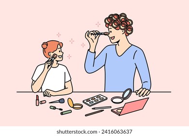 Mom and daughter do makeup together, preparing for family party, standing near table with cosmetics. Woman teaches little girl how to properly use cosmetics and apply makeup to face.