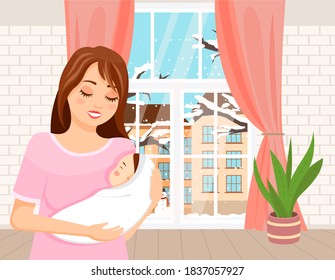 Mom Holding In Her Arms A Small Baby Is Standing In The Room. Newborn In A Tender Embrace Of Mother. Happy Young Woman With An Infant Is Standing Indoors Against A Window With A Winter Landscape