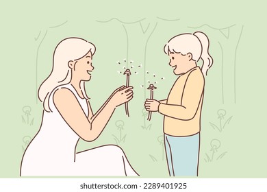 Mom and little daughter are holding dandelions, rejoicing at onset of spring and good hot weather. Caring woman teaches teenager girl with dandelions to love nature and take care of environment 