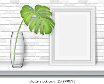 Monstera leaf and picture frame on a white table on brick wall background.