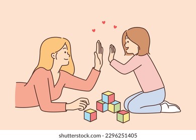 Mother and preschool daughter high-five, celebrating construction of tower of childrens blocks lying on floor. Caring mother woman raises child, involving in games that develop fine motor skills