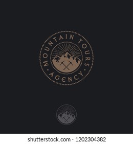 Mountain tours logo. Travel agency emblem. Gold mountains and ice axes on a circle. Emblem for alpinism, ski resort or mountain tourism. Monochrome option.